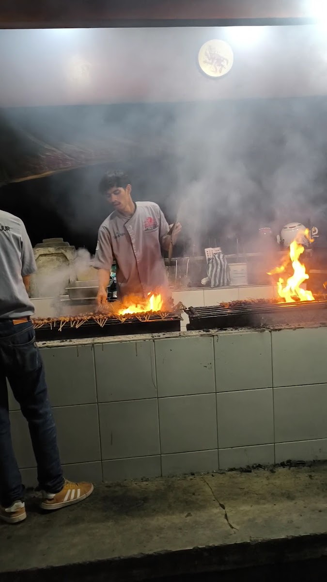 Juru bakar mengipasi tusukan sate di atas bara arang yang menyala di malam hari